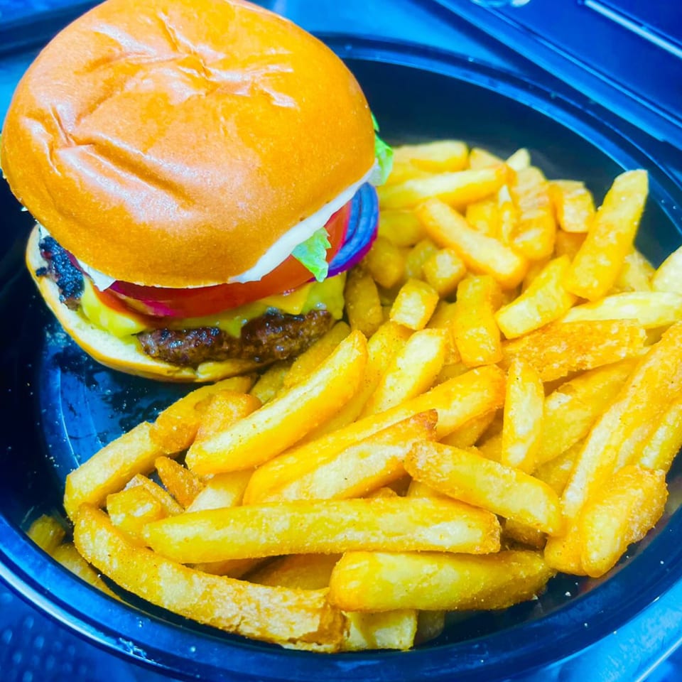 A K&S Caribbean Cuisine cheeseburger with lettuce, tomato, onion, and a side of fries.