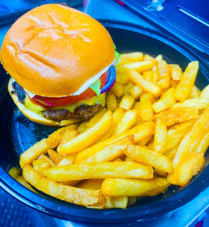 A K&S Caribbean Cuisine cheeseburger with lettuce, tomato, onion, and a side of fries.