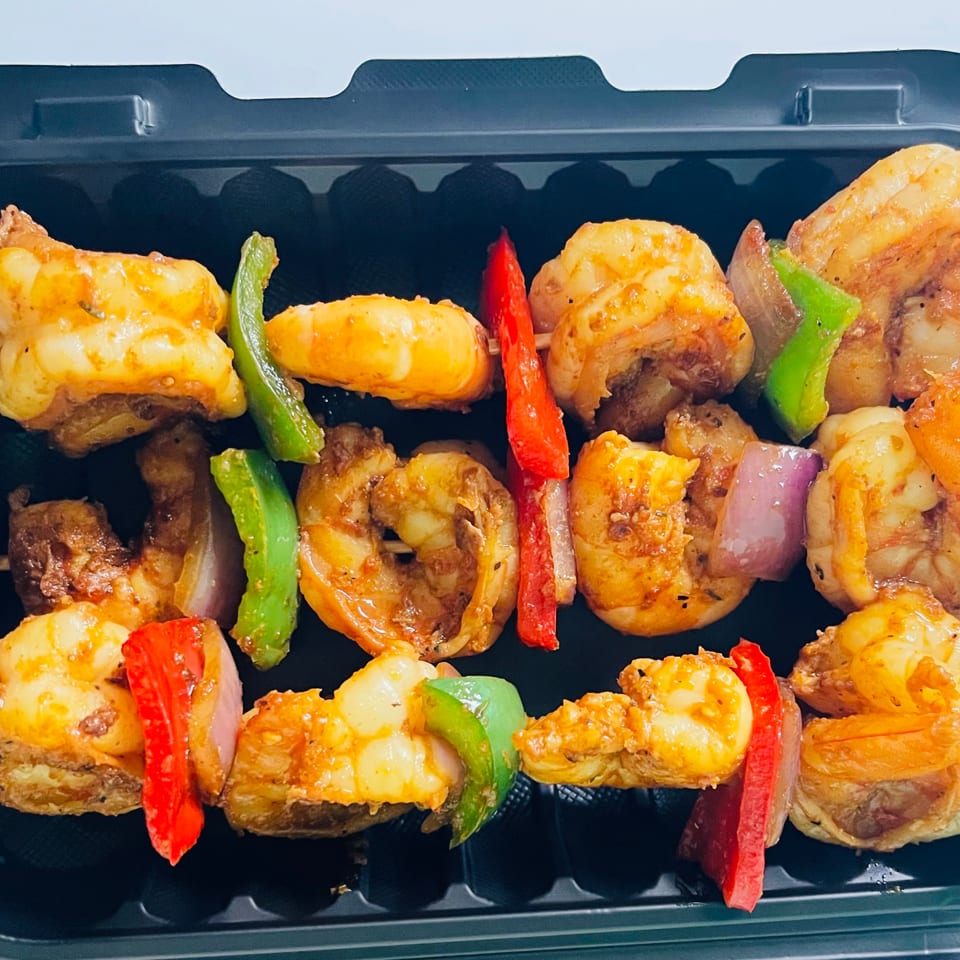 Three Caribbean shrimp and vegetable skewers with red and green peppers, and onions in a black container.